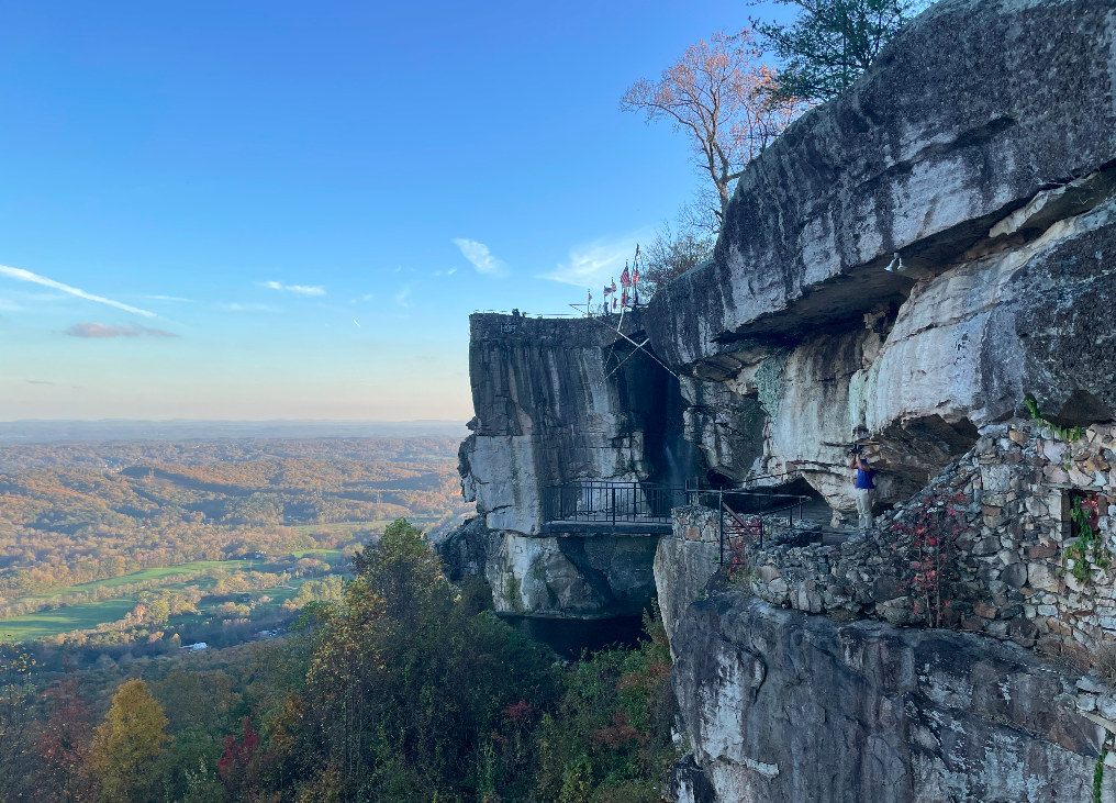 The Lover’s Leap overlook at Rock City: a rock promontory topped by a stone observation deck flying seven state flags, jutting from a limestone cliff face above a wooded valley.
